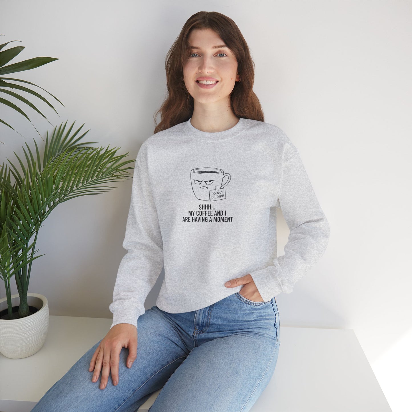 Woman wearing a light grey sweatshirt with a coffee cup graphic and text.