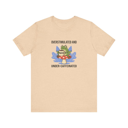 T-shirt graphic with frog on mushroom, holding coffee cup, text "Overstimulated and Under-caffeinated".