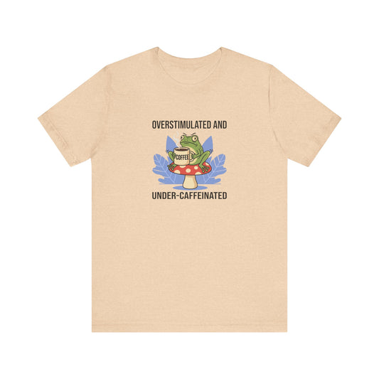T-shirt graphic with frog on mushroom, holding coffee cup, text "Overstimulated and Under-caffeinated".