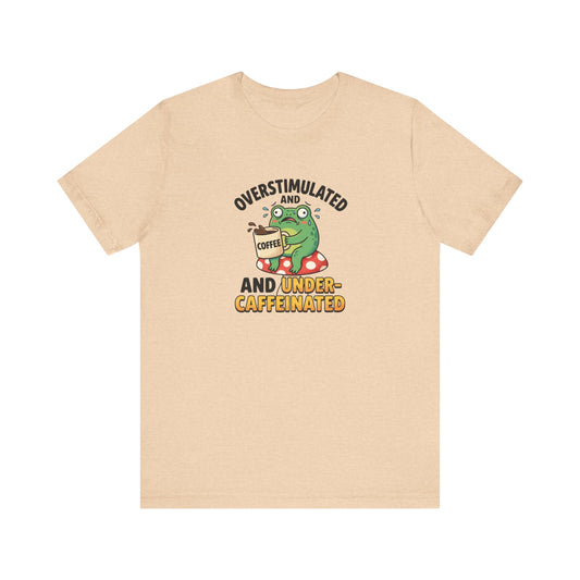 T-shirt graphic of a frog on a mushroom, holding coffee, with text "overstimulated and caffeinated".