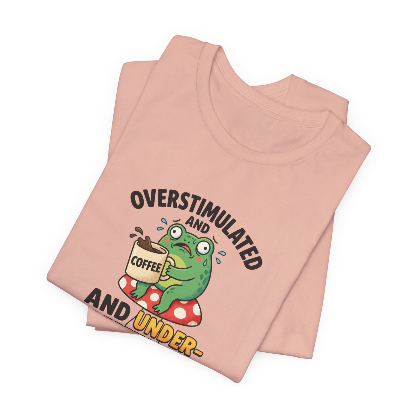 T-shirt with graphic of a frog holding a coffee cup, text reads "OVERSTIMULATED AND UNDER-".