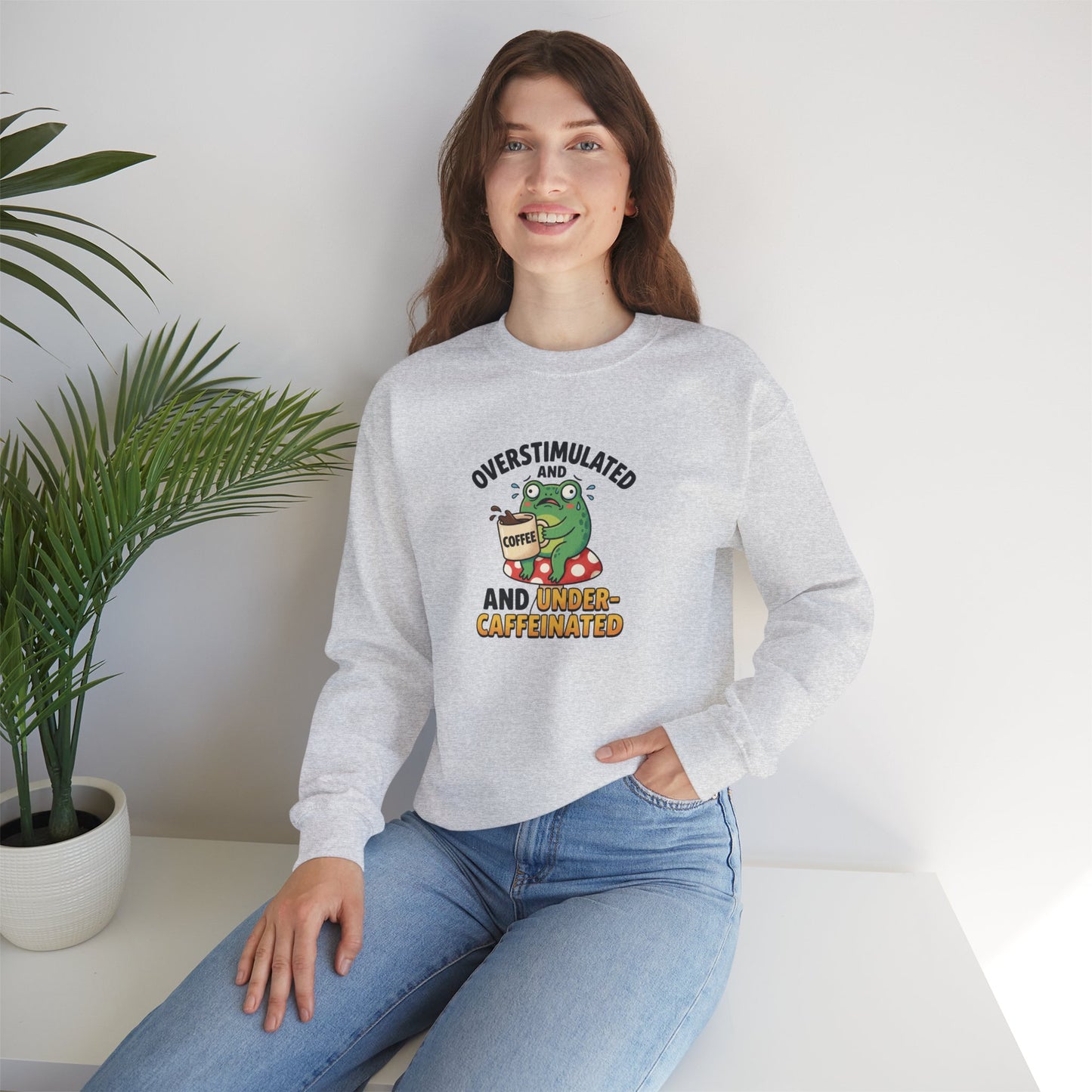 Light gray crewneck sweatshirt with a frog holding a coffee cup, text reads "overstimulated and under-caffeinated."